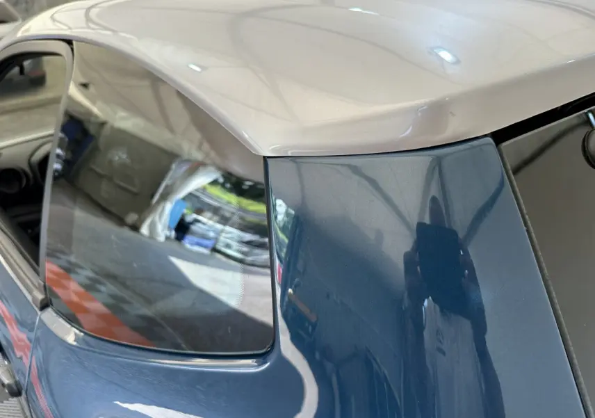 Vue rapprochée du côté arrière gauche de l’AIXAM Ambition bleu 2026 avec toit beige et vitre latérale teintée.