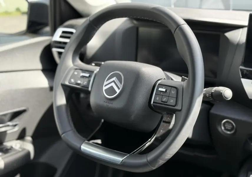 Vue rapprochée du volant cuir noir de la Citroën C4 Hybrid 2025 avec commandes intégrées et bouton de démarrage.