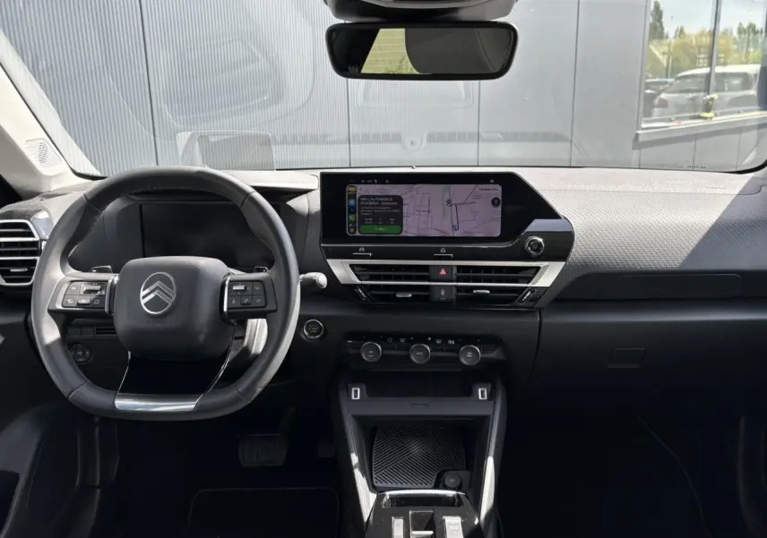 Vue intérieure avant du tableau de bord et volant noir de la Citroën C4 Hybrid 145 e-DSC6 Max avec écran tactile GPS allumé.