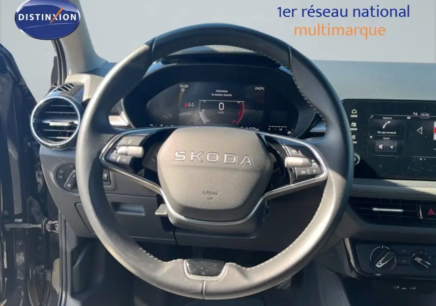 Vue intérieure centrée sur le volant SKODA d'une Fabia noire, avec tableau de bord numérique et écran tactile visible.