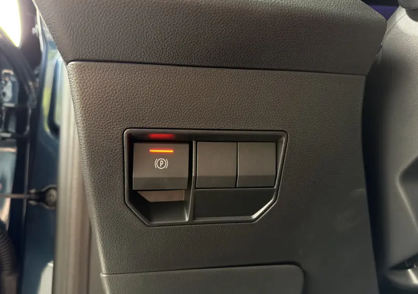 Gros plan sur le bouton de frein à main électrique allumé, côté gauche intérieur d'un Dacia Bigster Bleu Indigo 2026.