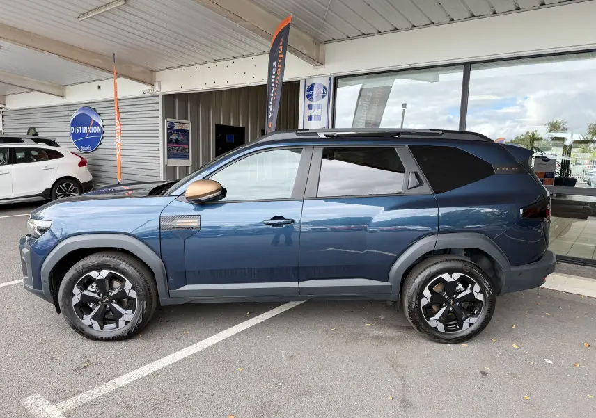 Vue de profil côté gauche du SUV Dacia Bigster Hybrid 155 Extreme bleu indigo avec jantes diamantées et rétroviseurs bronze.