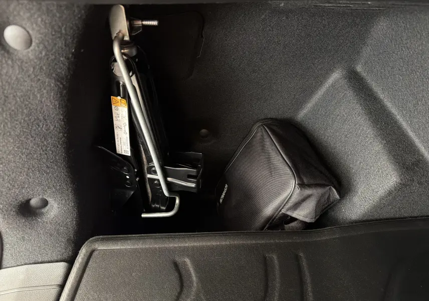 Coffre du Dacia Bigster Hybrid 155 Extreme 2026, vue intérieure montrant le cric et une trousse noire de secours.