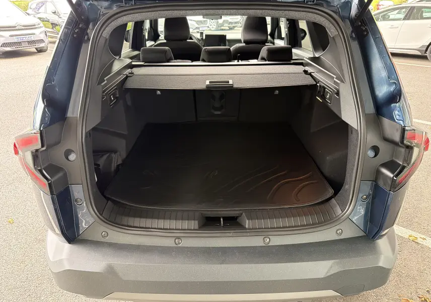 Vue arrière du coffre ouvert du Dacia Bigster Hybrid 155 Extreme bleu indigo, montrant l'espace de chargement et la plage arrière.