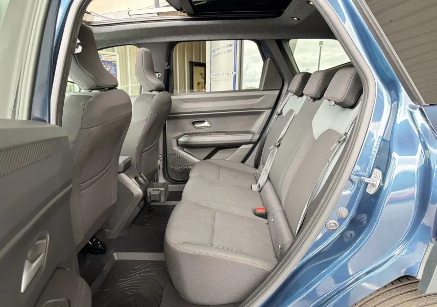 Vue intérieure côté droit de la banquette arrière du Dacia Bigster Hybrid 155 Extreme bleu indigo avec toit ouvrant panoramique.