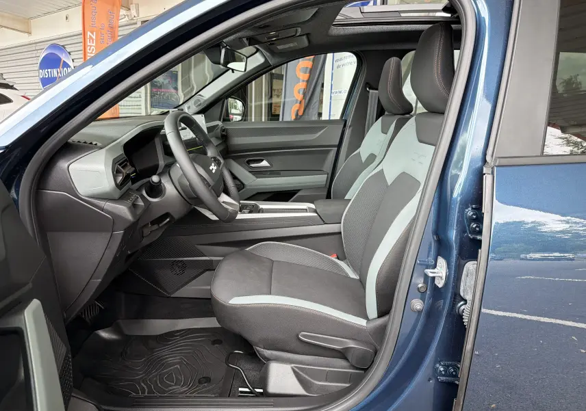 Vue intérieure côté conducteur du Dacia Bigster bleu indigo, mettant en valeur les sièges bicolores et le tableau de bord moderne.