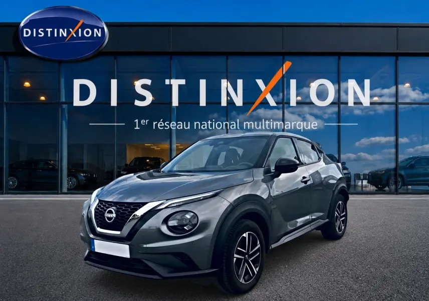 Nissan Juke gris 2025 en 3/4 avant droit, avec jantes alu et calandre noire brillante devant showroom Distinxion.