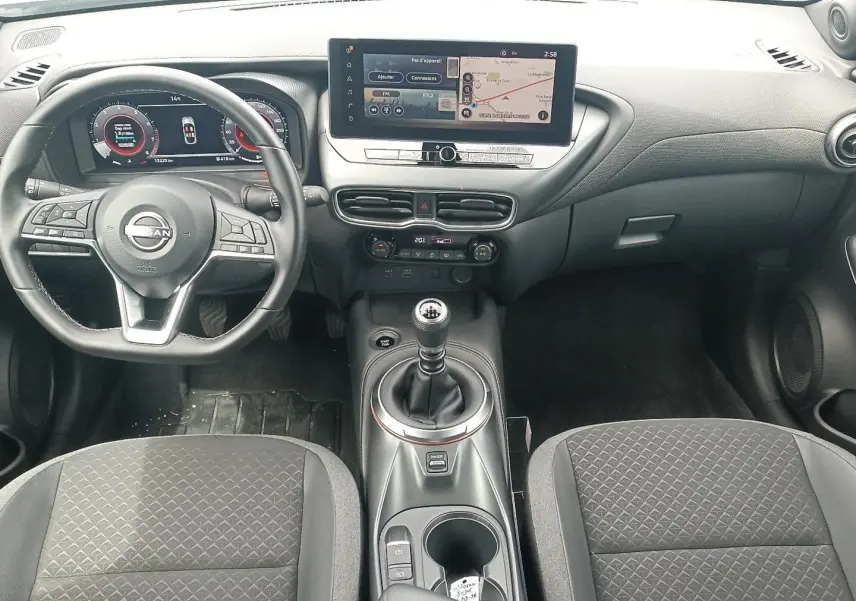 Vue intérieure avant du Nissan Juke 2025 avec tableau de bord numérique, écran tactile et levier de vitesse manuel.