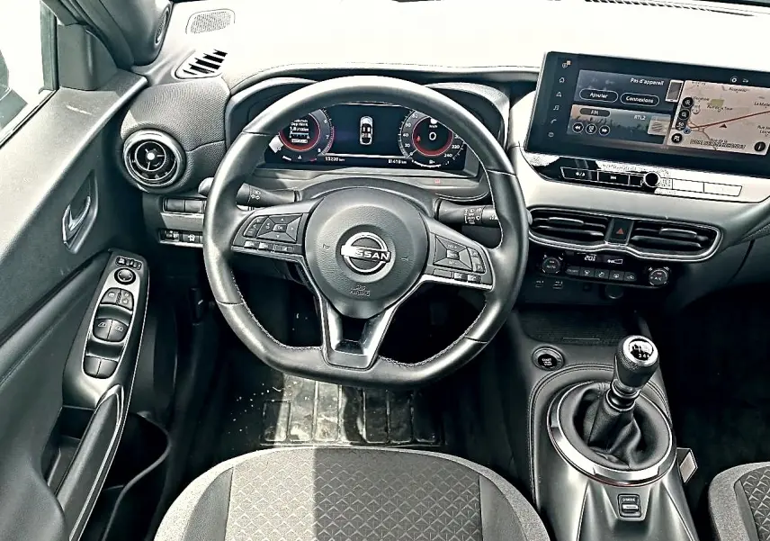 Vue intérieure centrée sur le volant cuir multifonction et la console avec boîte manuelle du Nissan Juke gris 2025.