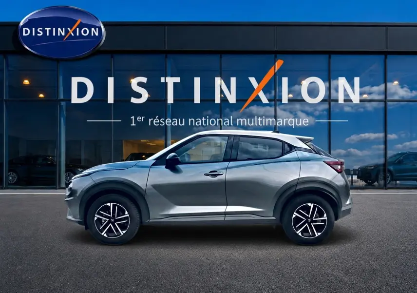 Nissan Juke gris vue de profil côté gauche, avec jantes alliage et toit blanc contrasté, devant une vitrine Distinxion.