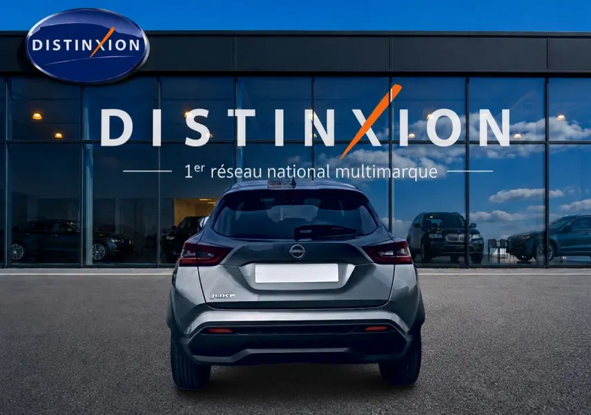 Vue arrière d'un Nissan Juke gris 2025 garé devant une vitrine avec logo Distinxion.