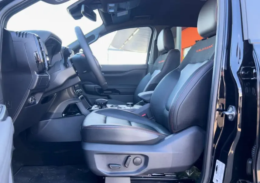 Vue côté conducteur intérieur du Ford Ranger Wildtrak 2026 noir agate, sièges cuir avec surpiqûres orange et logo Wildtrak.