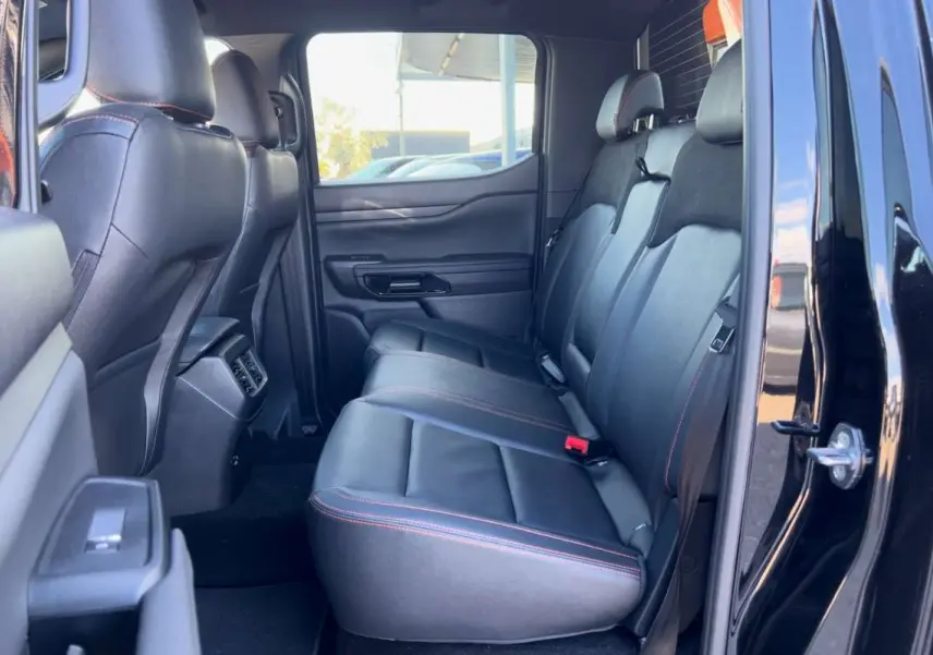 Vue intérieure arrière côté droit du Ford Ranger Wildtrak noir agate, montrant les sièges en cuir avec surpiqûres orange.