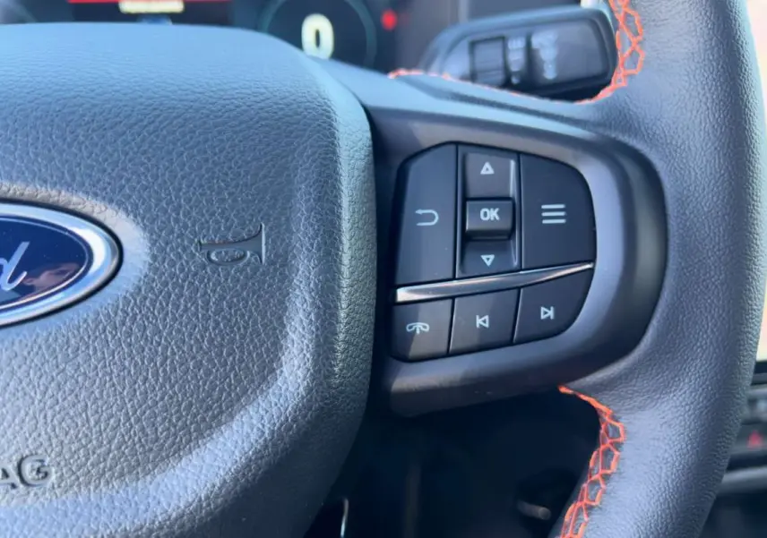 Gros plan sur le volant noir en cuir avec surpiqûres orange et commandes multifonctions du Ford Ranger 2026.