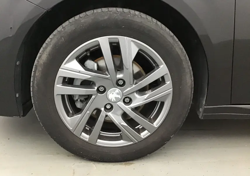 Gros plan sur la roue avant gauche d'une Peugeot 208 noire 2022 avec jante alliage gris et logo lion central.
