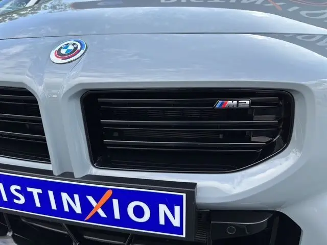 Gros plan sur la calandre avant gris Brooklyn Grau d'une BMW M2 G87 avec logo M2 et badge BMW visible.