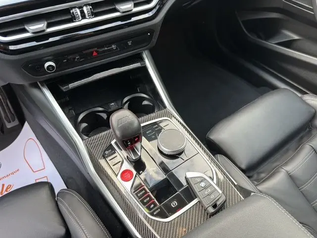 Vue rapprochée de la console centrale carbone avec levier de vitesse M et clé BMW posée, sièges cuir noir visibles.