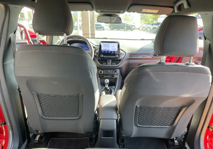 Vue intérieure arrière du Ford Puma rouge 2021, montrant les sièges avant noirs avec surpiqûres rouges et la console centrale avec écran tactile.
