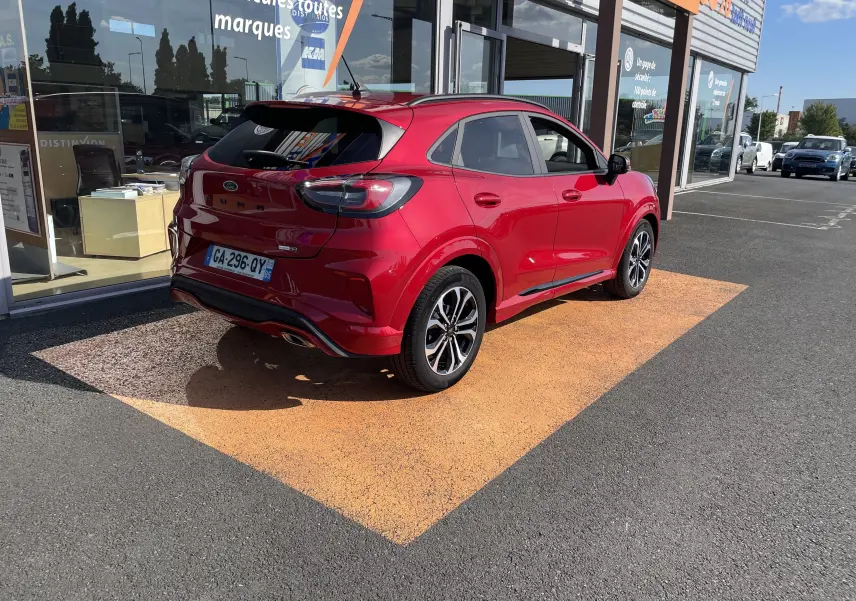 Ford Puma rouge vue 3/4 arrière droit, stationnée devant une vitrine avec jantes alliage bicolores et feux LED.