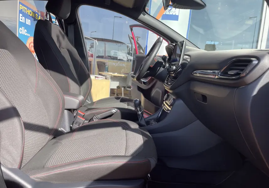 Intérieur du Ford Puma rouge 2021 vu côté conducteur, sièges tissu noir avec surpiqûres rouges et tableau de bord moderne.