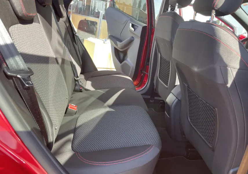 Vue intérieure arrière du Ford Puma rouge 2021, montrant les sièges arrière en tissu noir avec surpiqûres rouges et portières ouvertes.