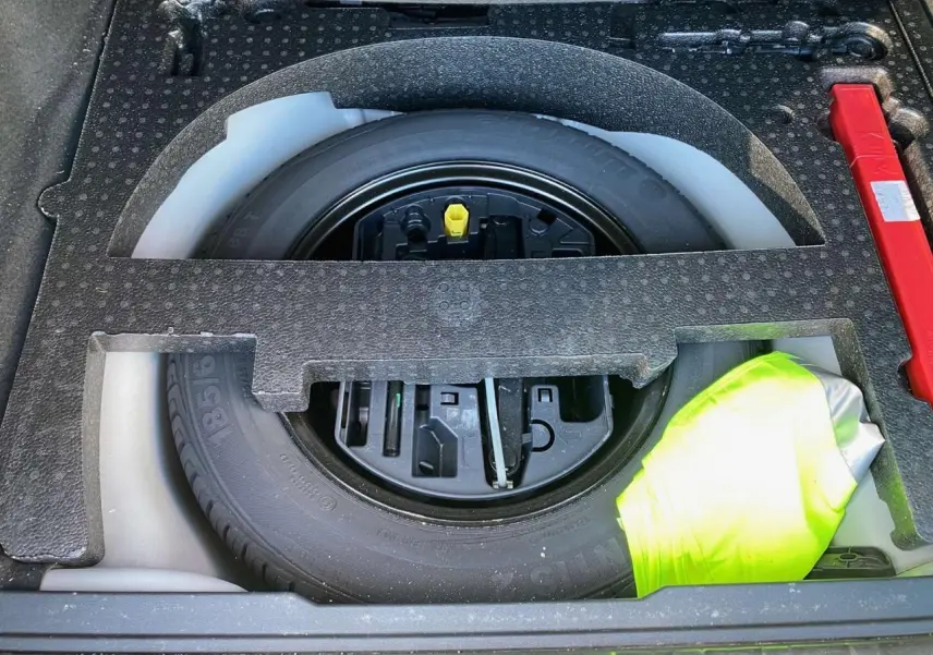 Vue rapprochée de la roue de secours en tôle noire dans le coffre du Peugeot 2008 2019 avec un gilet jaune visible.