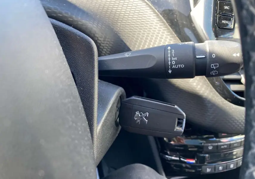 Gros plan sur la clé Peugeot insérée dans le contacteur, volant noir et commandes de lève-glace en arrière-plan.