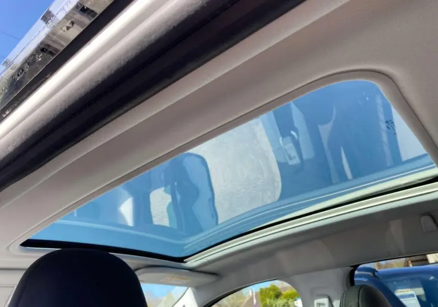 Toit vitré panoramique ouvert vu de l'intérieur arrière d'un Peugeot 2008 avec ciel bleu visible à travers le verre.