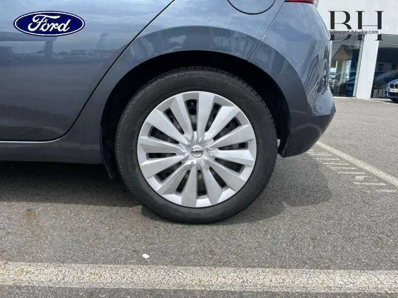 Gros plan sur la roue arrière droite d'une Nissan Micra gris acier, avec enjoliveur et partie de la carrosserie visible.
