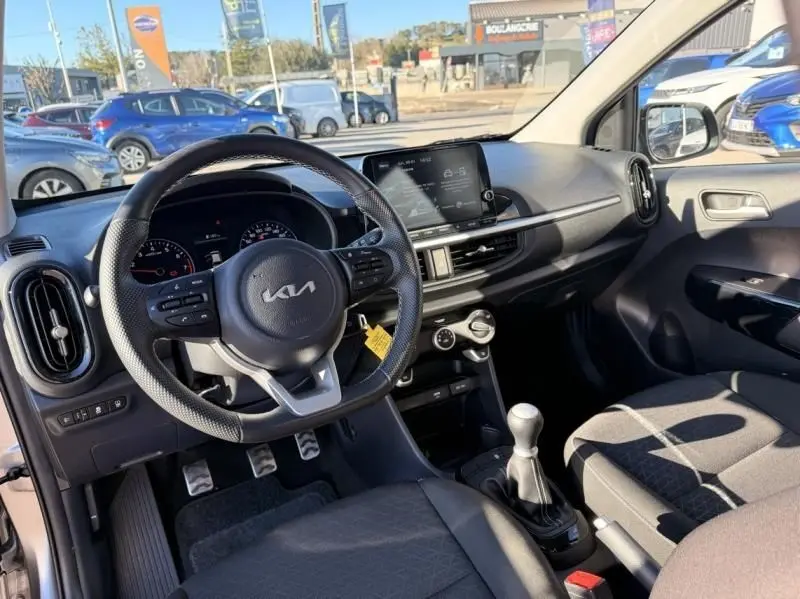 Intérieur de la Kia Picanto 2023 gris foncé, vue côté conducteur, volant multifonction et boîte manuelle visible.