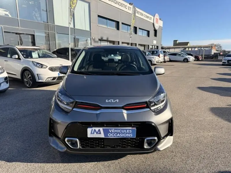 Vue avant d’une KIA Picanto 2023 gris foncé GT Line avec détails rouges sur la calandre, stationnée en extérieur.