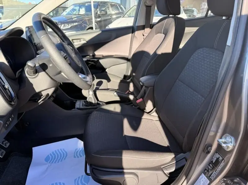 Vue intérieure côté conducteur de la KIA Picanto gris foncé 2023, montrant les sièges tissu et la boîte manuelle.