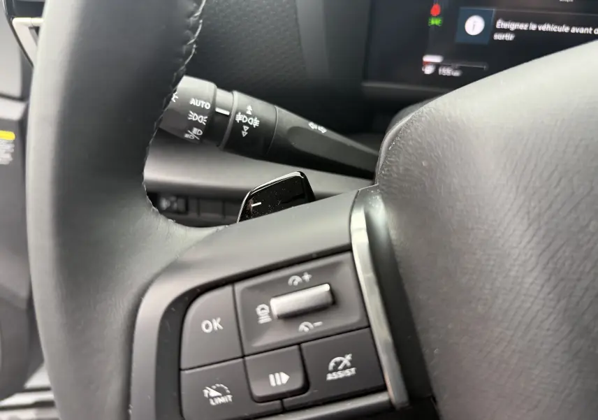 Gros plan sur les commandes au volant côté gauche du Citroën C4 Hybrid 145 e-DCS6 Max, intérieur noir avec affichage numérique partiel.