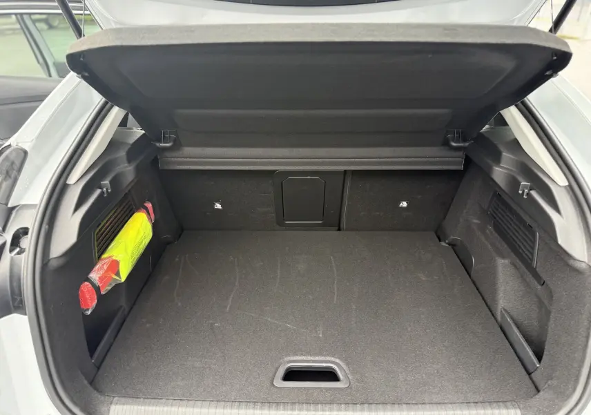 Coffre ouvert vu de l'arrière d'une Citroën C4 Hybrid 145 blanc Okenite, avec rangement noir et triangle de sécurité visible.