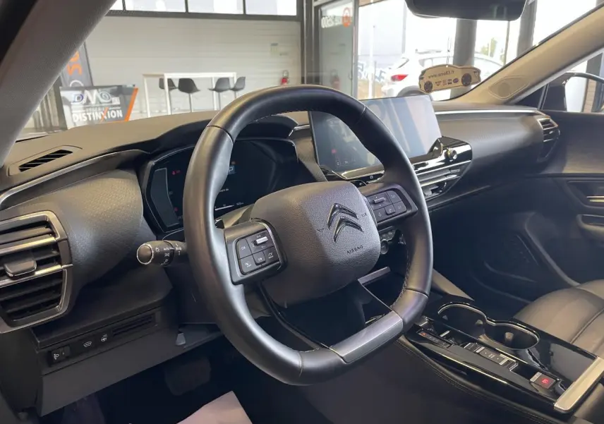Vue intérieure du poste de conduite du Citroën C5 X 2024, volant cuir noir et écran tactile central visible.