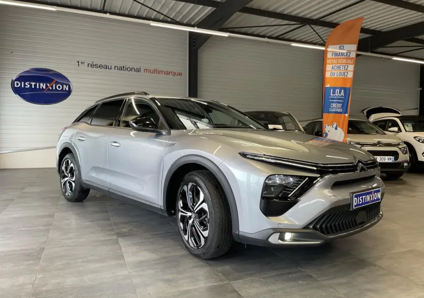 Vue 3/4 avant d'une Citroën C5 X 2024 gris foncé, avec jantes alliage et calandre distinctive dans un showroom.