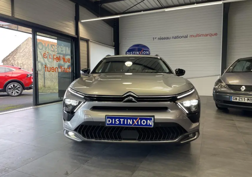 Vue avant d'un Citroën C5 X 2024 gris foncé avec calandre distinctive et phares allumés en showroom.