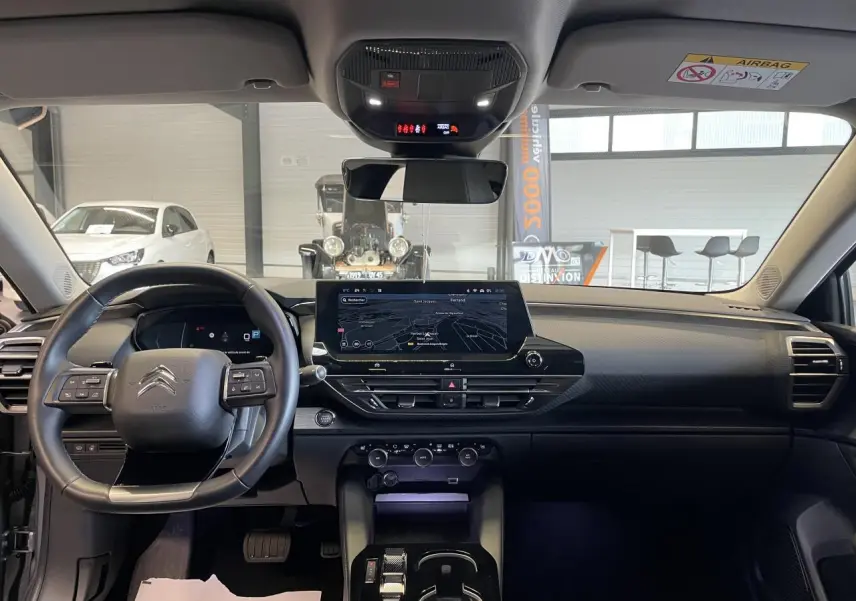 Vue intérieure frontale du tableau de bord noir de la Citroën C5 X 2024 avec écran tactile central et volant multifonction.