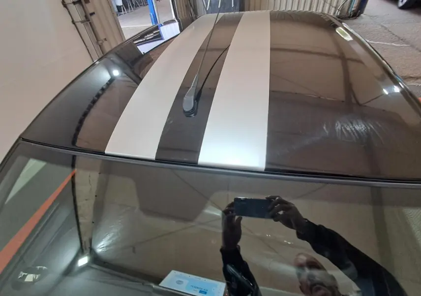 Vue plongeante sur le toit gris clair de l'AIXAM AMBITION 2024 avec bandes blanches sportives et antenne centrale.