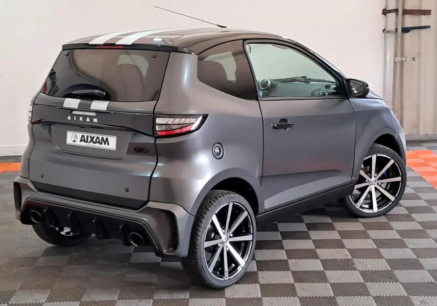 Vue 3/4 arrière droite de l’Aixam Ambition gris clair avec jantes alliage noires diamantées et bandes blanches sur le toit.