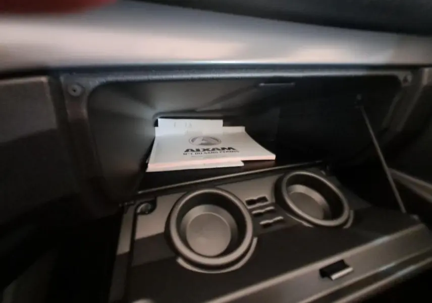 Intérieur de la boîte à gants ouverte de l'AIXAM Ambition 2024 avec porte-gobelets et documentation visible.