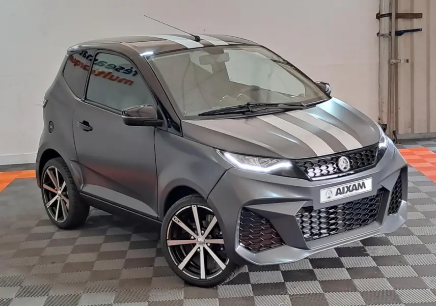 Aixam Ambition 2024 gris clair en 3/4 avant droit avec bandes blanches et jantes alliage noires diamantées.
