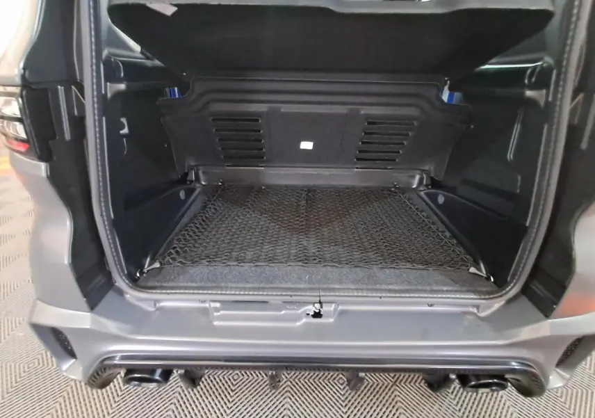 Coffre ouvert vu de l'arrière d'une Aixam Ambition gris clair, avec filet de rangement et pare-chocs sport visible.