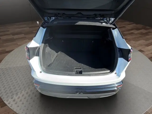 Vue arrière d’un Renault Austral blanc nacré avec hayon motorisé ouvert, toit noir visible, coffre spacieux et vide.