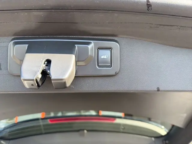 Gros plan sur le bouton d'ouverture du hayon motorisé du Renault Austral 2025, intérieur noir du coffre visible.