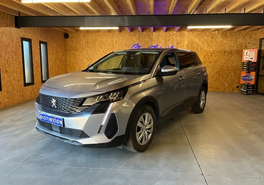 Peugeot 5008 gris en 3/4 avant droit dans un showroom avec éclairage intérieur et mur en bois.