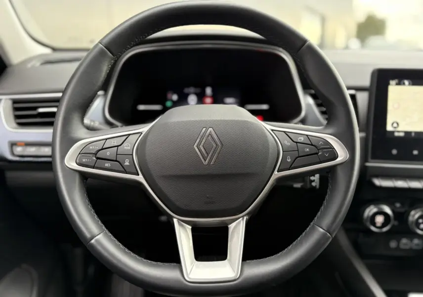 Vue rapprochée du volant en cuir noir avec commandes intégrées du Renault Arkana 2025, intérieur moderne et écran tactile visible.