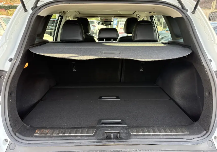 Vue arrière du coffre ouvert d’un Renault Kadjar blanc 2015, montrant l’espace de chargement avec cache-bagages en place.