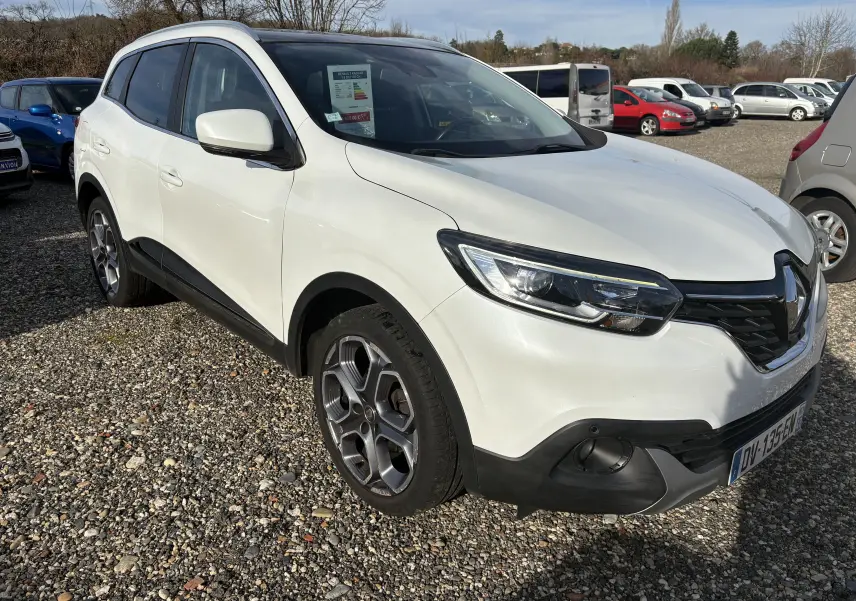 Renault Kadjar blanc en 3/4 avant droit sur parking, avec jantes alliage et calandre noire distinctive.