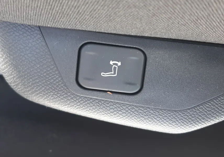 Bouton noir de réglage électrique du siège arrière, avec pictogramme blanc, sur garniture intérieure grise.